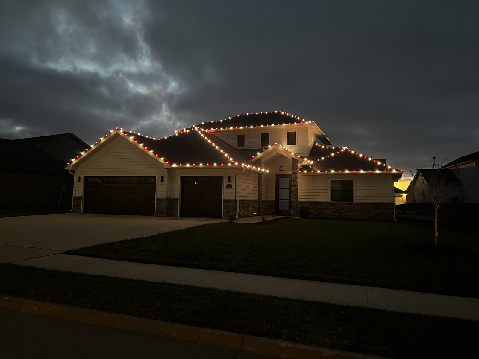 Warm Christmas lights outlining a home under an evening sky